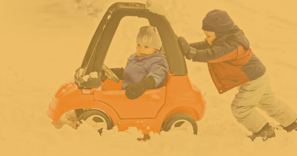 young student pushes another young student in a toy car through the snow.